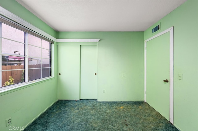 unfurnished bedroom with a closet, dark carpet, and visible vents