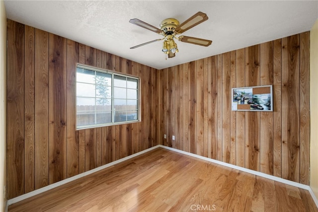 spare room featuring wood walls, wood finished floors, a ceiling fan, and baseboards