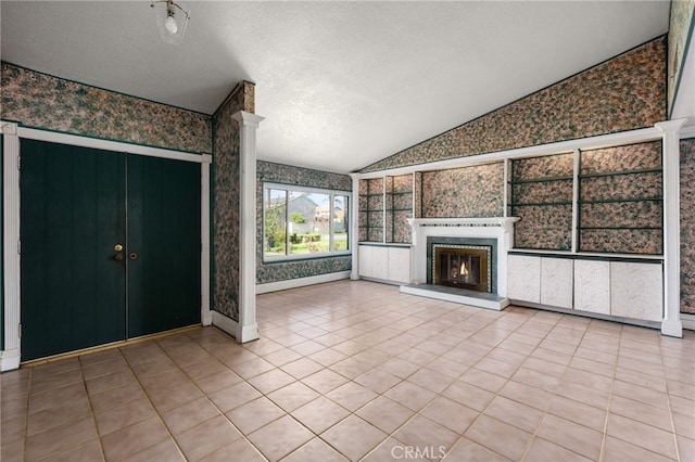 unfurnished living room with lofted ceiling, a glass covered fireplace, a textured ceiling, baseboards, and wallpapered walls