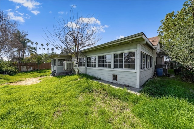 rear view of property with cooling unit, fence, and a lawn