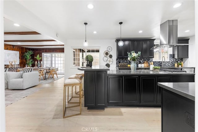 kitchen with tasteful backsplash, hanging light fixtures, light hardwood / wood-style flooring, island exhaust hood, and beam ceiling