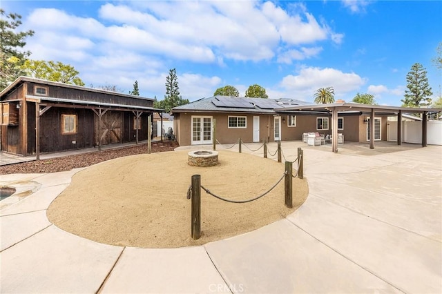 rear view of house featuring a patio area, solar panels, and an outdoor fire pit