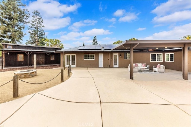 back of property featuring solar panels, a patio area, and an outdoor living space with a fire pit