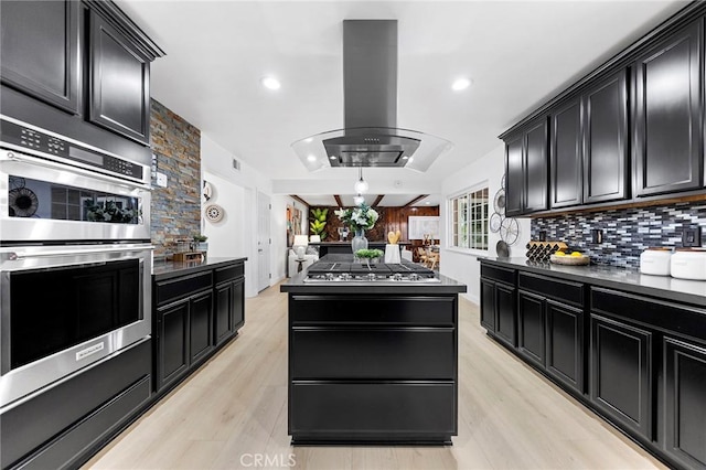 kitchen featuring light wood-type flooring, a kitchen island, island exhaust hood, stainless steel appliances, and backsplash