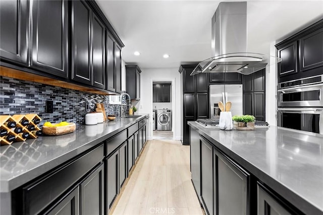 kitchen featuring sink, tasteful backsplash, island range hood, washer and dryer, and appliances with stainless steel finishes