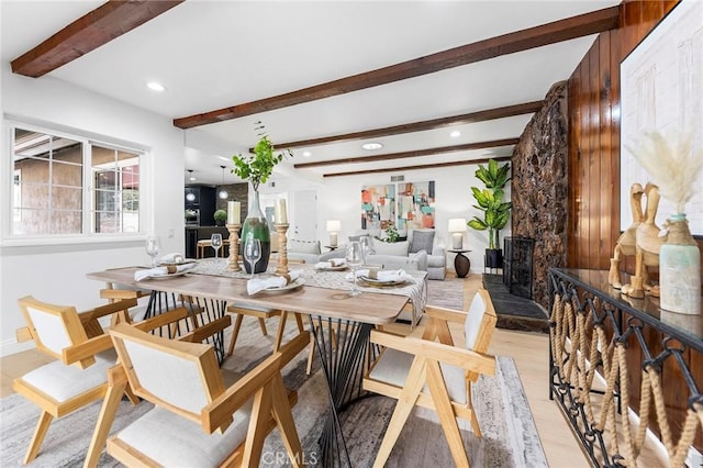 dining space with a stone fireplace, beam ceiling, and light wood-type flooring