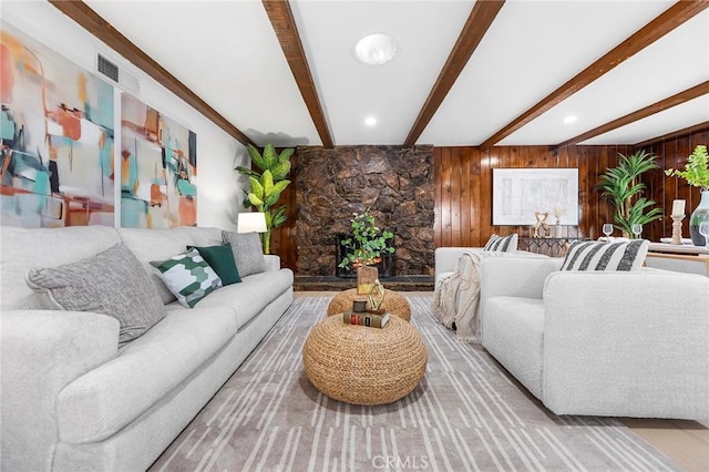 living room featuring a stone fireplace, wooden walls, and beamed ceiling