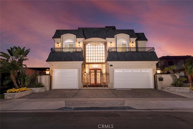 french provincial home with mansard roof, decorative driveway, a balcony, and stucco siding