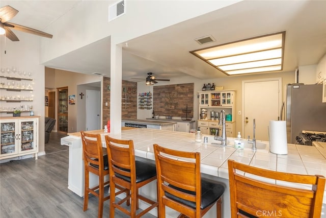 kitchen with tile countertops, white cabinetry, stainless steel fridge, dark hardwood / wood-style flooring, and a kitchen bar