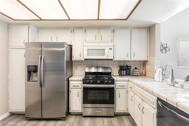 kitchen with tile countertops, sink, white cabinets, stainless steel appliances, and light wood-type flooring