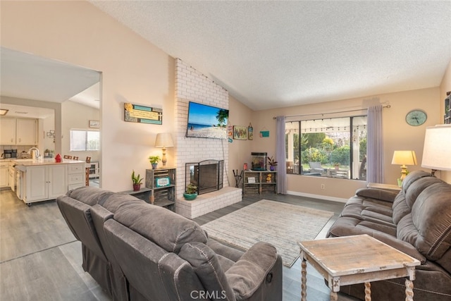 living room with lofted ceiling, sink, a brick fireplace, a textured ceiling, and light hardwood / wood-style floors