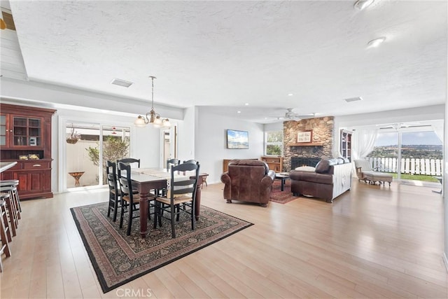 dining room featuring a stone fireplace, plenty of natural light, light hardwood / wood-style floors, and a textured ceiling