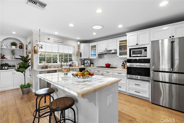 kitchen with appliances with stainless steel finishes, white cabinetry, a kitchen bar, a center island, and light stone countertops