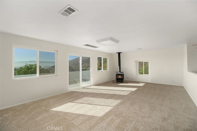 unfurnished living room with light colored carpet and a wood stove