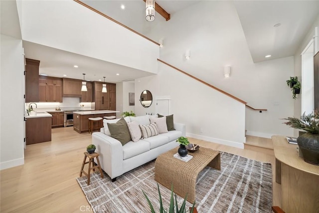 living room featuring a towering ceiling, sink, and light wood-type flooring