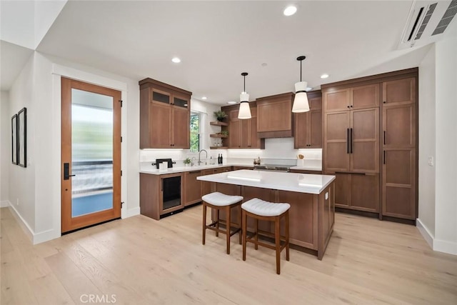 kitchen with a kitchen island, pendant lighting, sink, backsplash, and light wood-type flooring