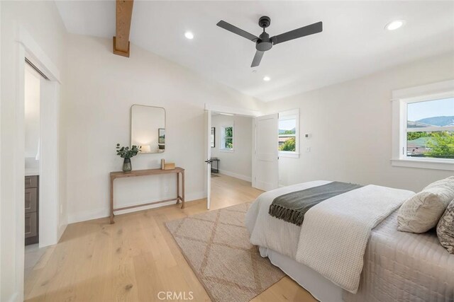 bedroom featuring multiple windows, vaulted ceiling with beams, ceiling fan, and light wood-type flooring