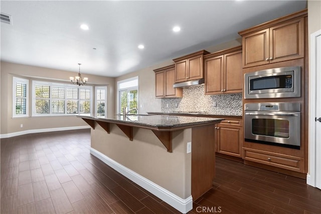 kitchen featuring appliances with stainless steel finishes, tasteful backsplash, a breakfast bar area, hanging light fixtures, and a kitchen island with sink