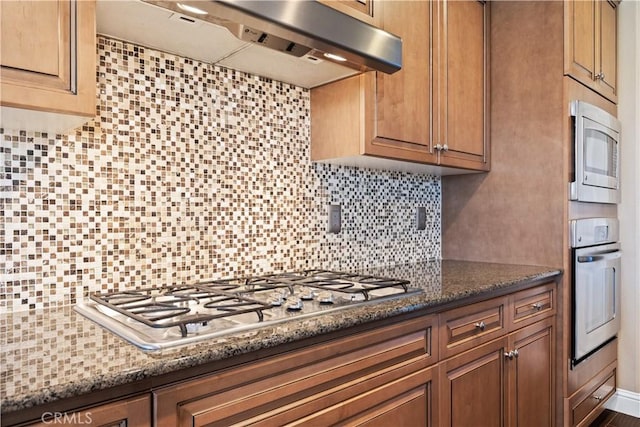 kitchen featuring dark stone countertops, stainless steel appliances, tasteful backsplash, and exhaust hood