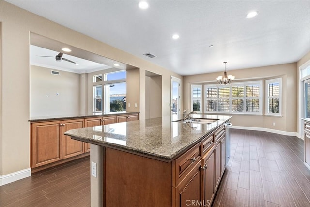 kitchen featuring sink, an inviting chandelier, stone countertops, decorative light fixtures, and an island with sink