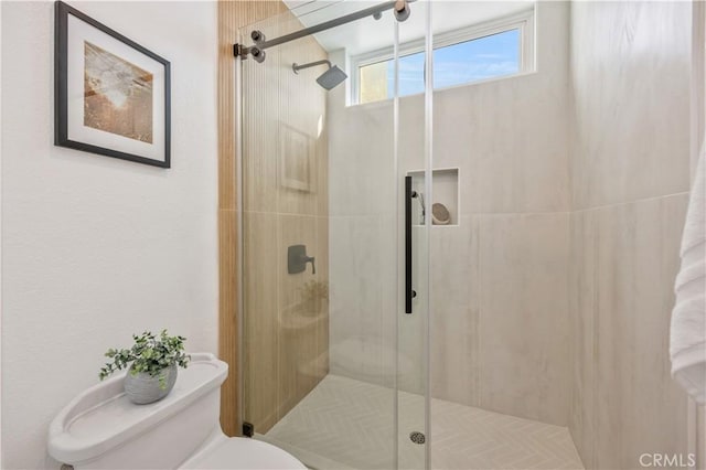 bathroom featuring a shower with door and toilet