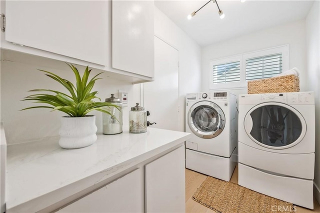 clothes washing area with independent washer and dryer, light hardwood / wood-style flooring, and cabinets