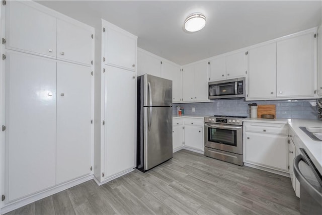 kitchen featuring stainless steel appliances, tasteful backsplash, white cabinets, and light wood-type flooring