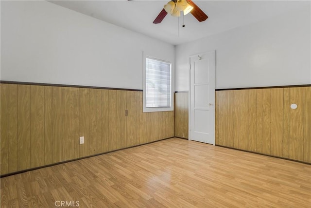 spare room with light wood-style floors, wooden walls, a ceiling fan, and wainscoting