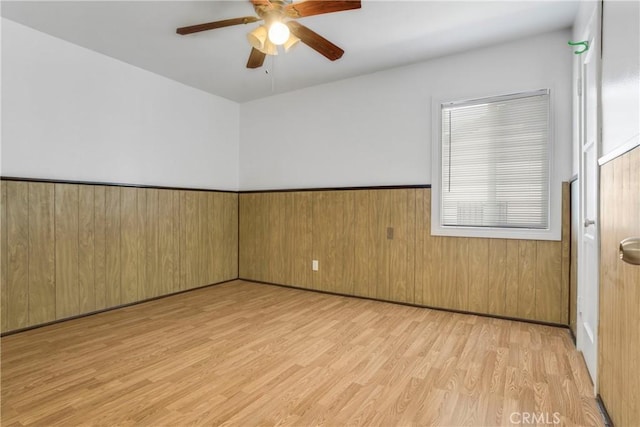 spare room with light wood finished floors, wainscoting, a ceiling fan, and wooden walls