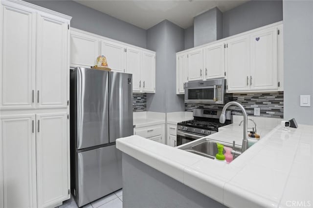 kitchen with tasteful backsplash, appliances with stainless steel finishes, tile counters, and white cabinets