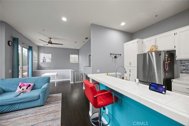 kitchen featuring dark wood-type flooring, stainless steel refrigerator, white cabinetry, backsplash, and tile counters