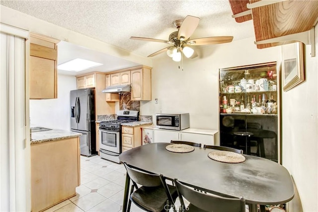 kitchen featuring stainless steel appliances, ceiling fan, light brown cabinets, and a textured ceiling