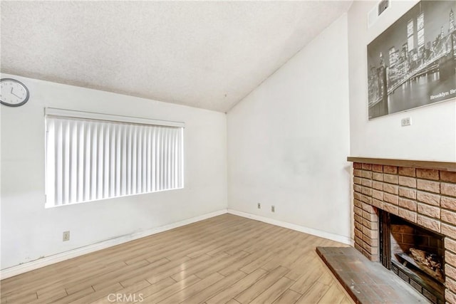 unfurnished living room with vaulted ceiling, a brick fireplace, a textured ceiling, and light hardwood / wood-style flooring