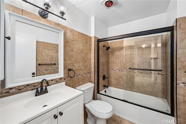 full bathroom with tile patterned floors, toilet, bath / shower combo with glass door, tile walls, and vanity