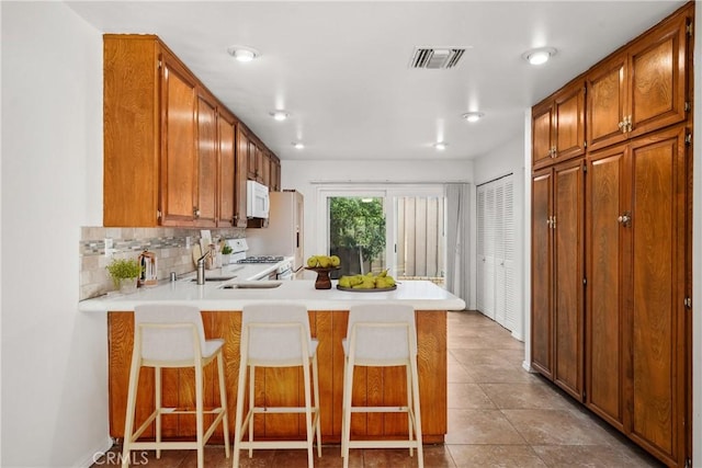 kitchen with tasteful backsplash, a breakfast bar, white appliances, and kitchen peninsula