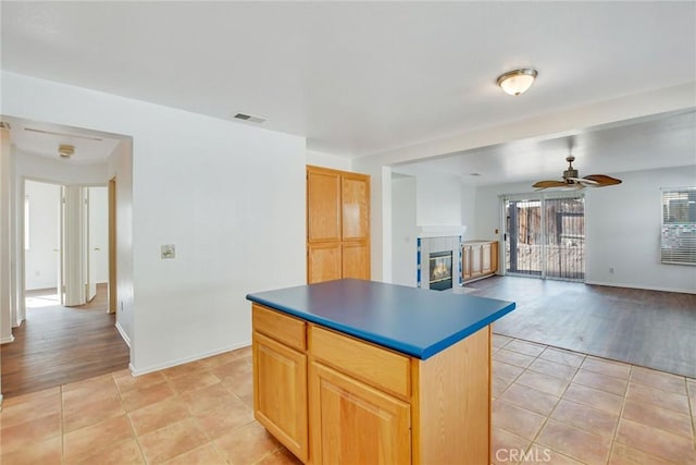 kitchen featuring light tile patterned floors, a tile fireplace, ceiling fan, and a kitchen island