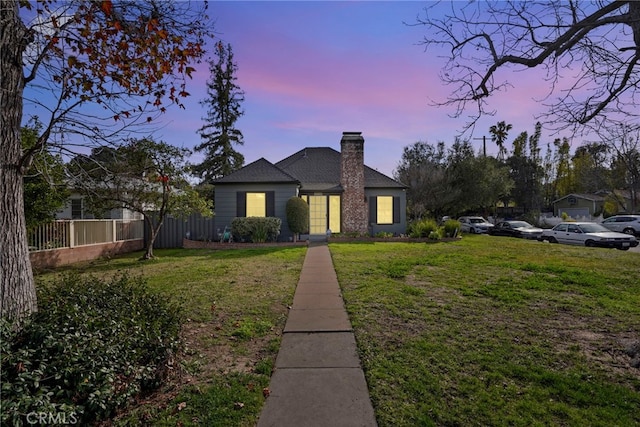 view of front of home featuring a chimney, fence, and a lawn