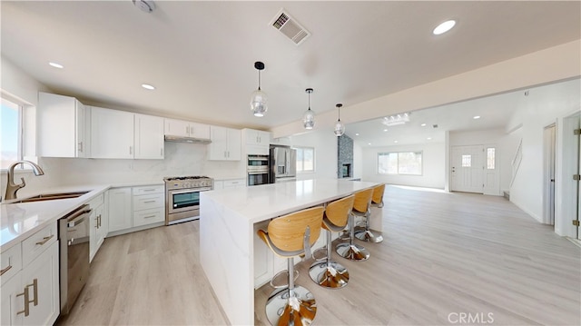 kitchen with appliances with stainless steel finishes, white cabinets, decorative light fixtures, a breakfast bar, and sink