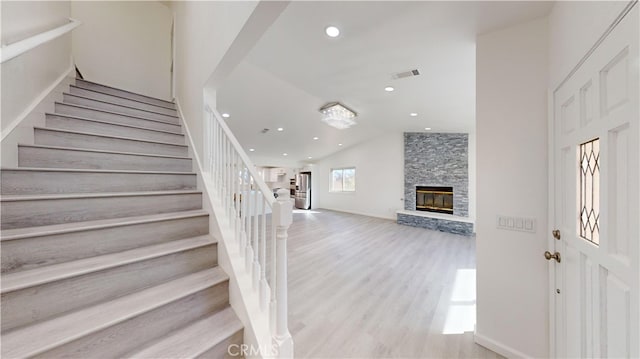 stairway featuring lofted ceiling, wood-type flooring, and a stone fireplace