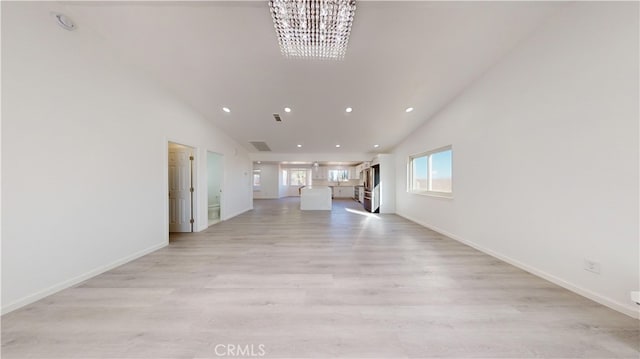 unfurnished living room featuring high vaulted ceiling, light hardwood / wood-style floors, and an inviting chandelier