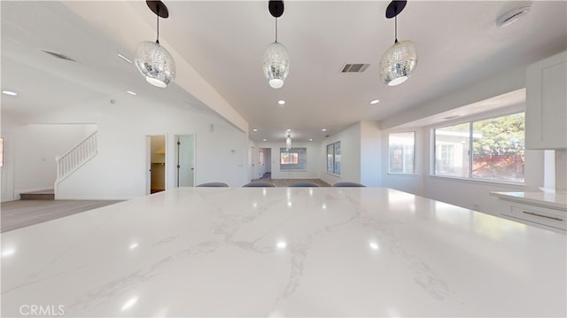 kitchen with decorative light fixtures, light stone counters, and white cabinetry