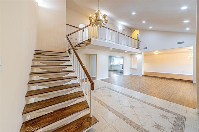 stairway with an inviting chandelier, tile patterned floors, and high vaulted ceiling