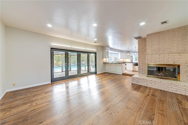 unfurnished living room with wood-type flooring, a brick fireplace, and french doors