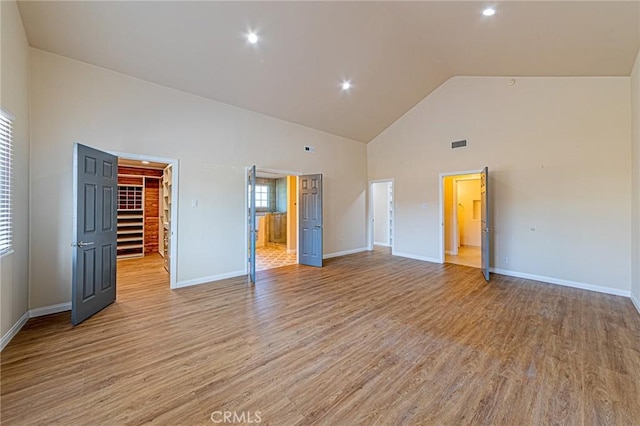 unfurnished bedroom with a spacious closet, high vaulted ceiling, and light hardwood / wood-style flooring