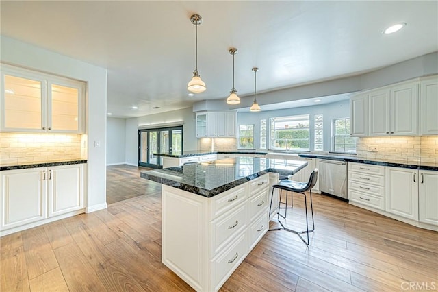 kitchen with hanging light fixtures, white cabinets, stainless steel dishwasher, dark stone counters, and light wood-type flooring