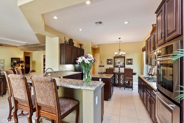 kitchen featuring sink, appliances with stainless steel finishes, hanging light fixtures, light stone countertops, and kitchen peninsula