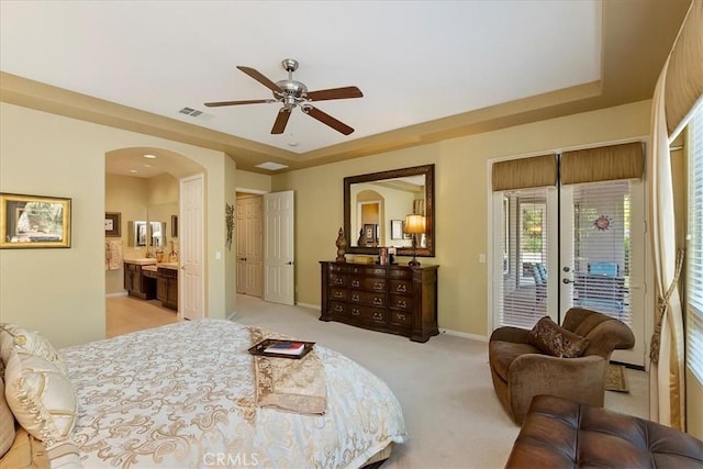 carpeted bedroom with ensuite bathroom, access to exterior, ceiling fan, a raised ceiling, and french doors