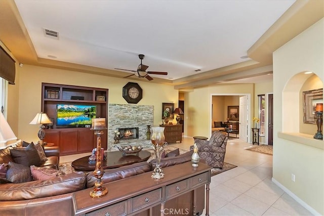 living room with light tile patterned flooring, ceiling fan, and a stone fireplace