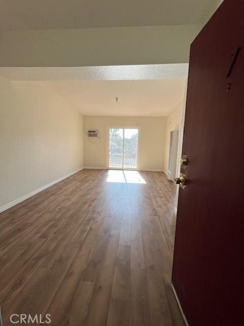 unfurnished room featuring a wall mounted AC, baseboards, and wood finished floors