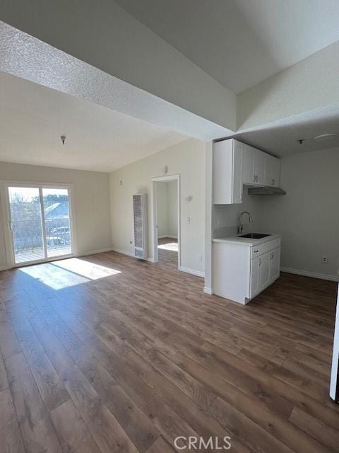 unfurnished living room featuring dark wood-style flooring, a sink, and baseboards